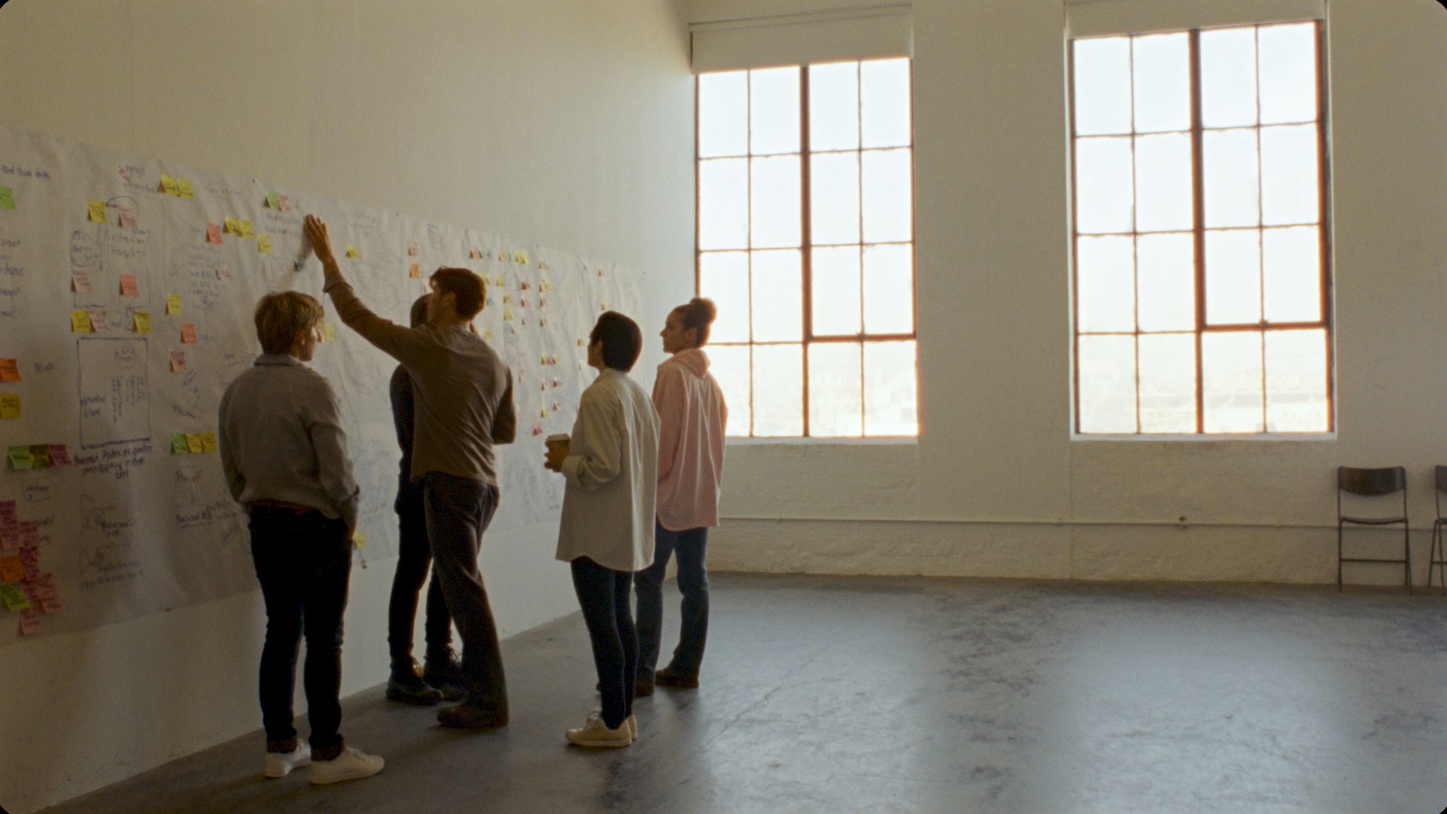 Colleagues standing at a studio wall of butcher paper and sticky notes, mid-session